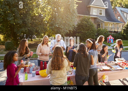 Neighbours talk and eat around a table at a block party Stock Photo
