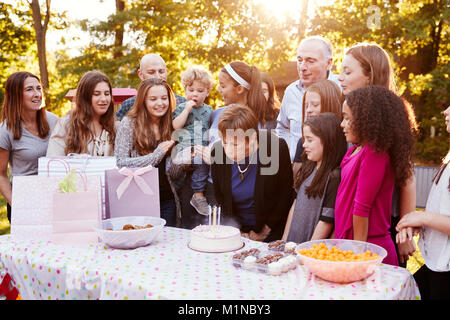 Senior woman blows out candles at her birthday garden party Stock Photo