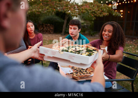 Teenage friends sitting at fire pit sharing take-away pizzas Stock Photo