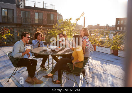 Five friends sitting at a table on a rooftop making a toast Stock Photo