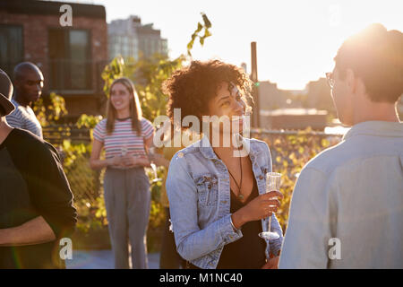Friends talking at a rooftop party backlit by sunlight Stock Photo