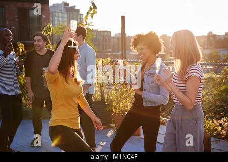 Female friends dancing and drinking at a rooftop party Stock Photo