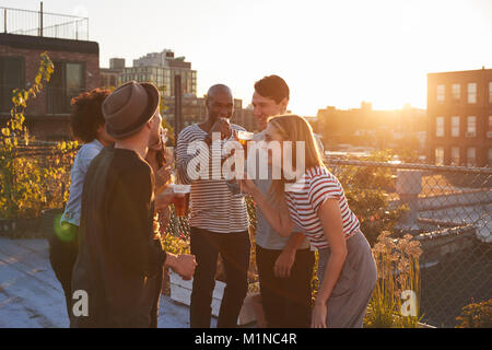 Friends stand talking at rooftop party, backlit by sunlight Stock Photo