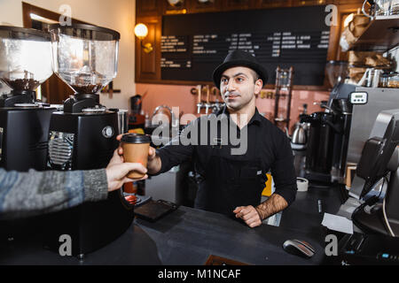 Positive barista male selling coffee to a consumer in a coffee shop. Stock Photo