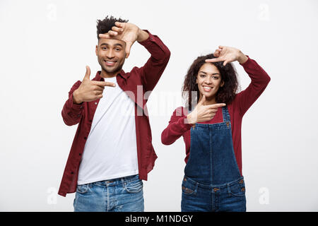 Happy young African American couple looking through a finger frame and smiling while standing isolated on white. Stock Photo