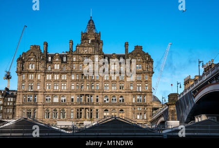 Rocco Forte Balmoral Hotel, Princes Street, Edinburgh, UK, with Waverley Station roof in front, and blue sky, cranes in distance Stock Photo