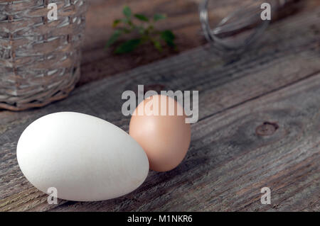 Goose and hen eggs on wooden table with basket and whip Stock Photo