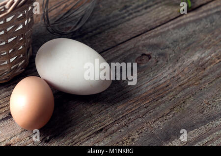 Goose and hen eggs on wooden table with basket and whip Stock Photo