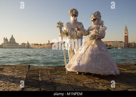 Couple of Venetian Masks in white drasses, Venice Carnival with Venice in background, island San Giorgio, Venice, Italy Stock Photo