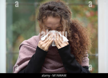 Outdoor portrait of a woman blowing her nose in paper tissue