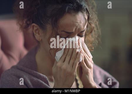 Closeup portrait of a woman with a miserable sick expression blowing her runny nose in a paper tissue Stock Photo