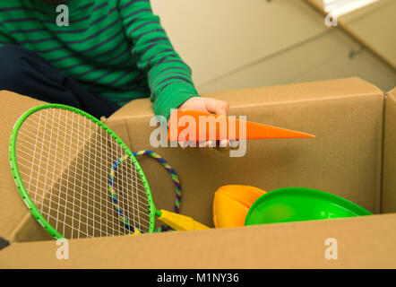 A child finding a wedge in a box of sporting goods and toys Stock Photo