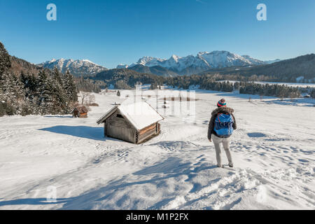 Woman standing in a snow-covered landscape,frozen Geroldsee in winter,small hay yard,Mittenwald,Karwendel,Upper Bavaria Stock Photo