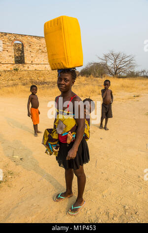 Woman with her baby on her back carrying a water canister on her head, Massangano, Cuanza Norte, Angola, Africa Stock Photo