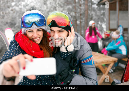 Smiling couple taking selfie together with cell phone in snowy mountain Stock Photo