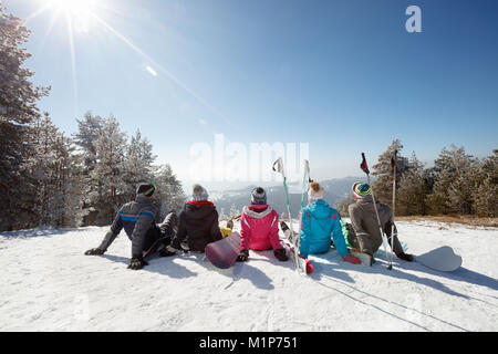 Skiers sitting on snow and looking landscape on skiing in mountain, back view Stock Photo
