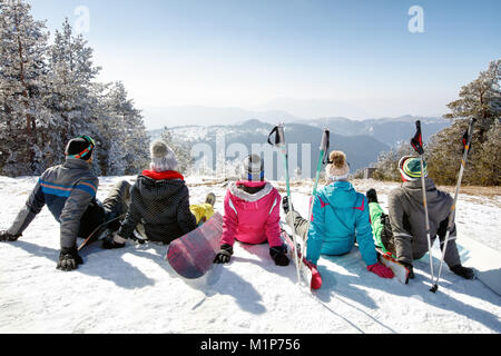 Group of skiers sitting on snow and looking beautiful landscape, back view Stock Photo