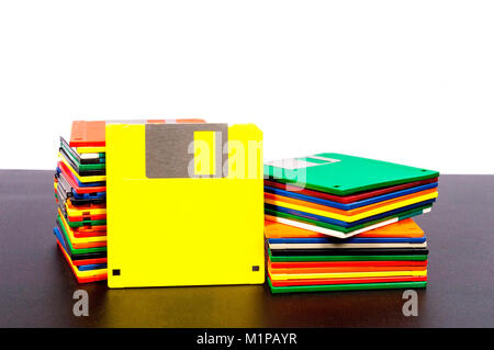 Horizontal shot of two stacks of old plastic disks with a yellow disk standing up against one stack.  Front side showing.  Dark table surface and whit Stock Photo