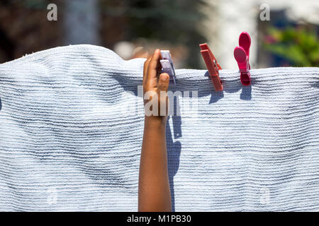 A young girl playing with clothes pegs and hanging a laundry blanket on a washing line in the garden. Stock Photo