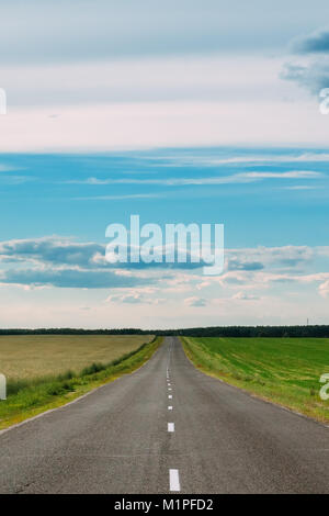 A direct asphalt road in the green fields on the rural background of the sky and clouds. Nobody Stock Photo