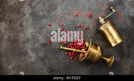 Pink pepper seeds, a brass pepper mill and a mortar on metal rusty background, top view, copy space Stock Photo