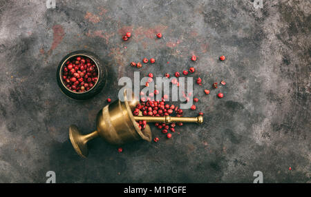 Pink pepper seeds and a brass mortar on metal rusty background, top view, copy space Stock Photo