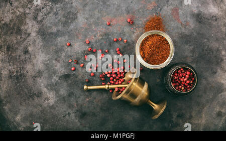 Pink pepper seeds and powder and a brass mortar on metal rusty background, top view, copy space Stock Photo