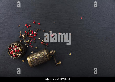 Various pepper seeds and a brass pepper mill on black stone background, top view, copy space Stock Photo