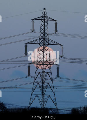 The full moon is visible through electricity pylons as it goes down near Larbert, Central Scotland. Stock Photo
