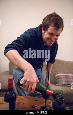 A smiling young man pouring a glass of red wine in a house Stock Photo