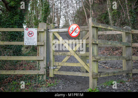 A wooden fence gate leading into woods with two signs: no cycling and no dogs except guide dogs, the latter featuring Welsh as well Stock Photo