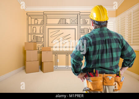 Contractor Standing Indoors with Moving Boxes Looking At Line Drwaing of Entertainment Unit on Wall. Stock Photo