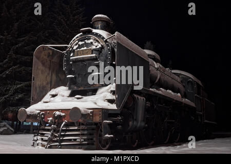 An old steam engine on display at the rural town of Oulainen in the Northern Finland. The engine has been covered by the winter snow. Stock Photo