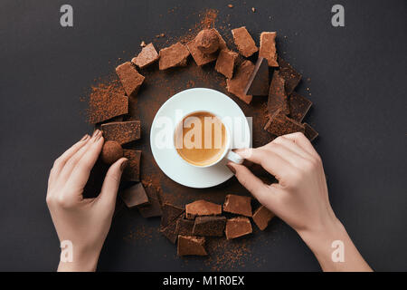 cropped shot of female hands, cup of coffee, truffles and chocolate on grey surface Stock Photo