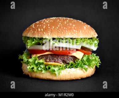 Delicious burger, hamburger or cheeseburger with sesame seed bun and fresh ingredients. Isolated on black background. Gourmet burger with fresh salad. Stock Photo