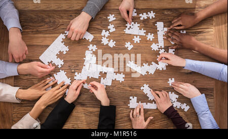 High Angle View Of Businesspeople Hand Solving Jigsaw Puzzle On Wooden Desk Stock Photo