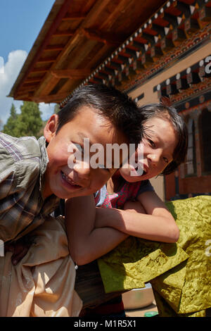 Boy and girl perching on fence of house and smiling in Bhutan Stock Photo