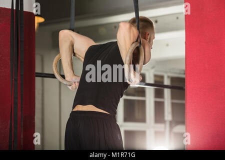 Young Fit Man Pulling Up On Gymnastic Rings In The Gym Stock Photo