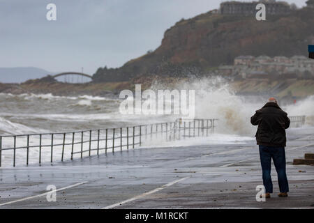 Colwyn Bay, Conwy County, Wales, UK UK Weather: Cold weather with high tide and windy weather have provided ideal conditions for Natural Resources Wales to provide flood warnings for the North Wales Coast including Colwyn Bay. A person storm watching along the promenade at Colwyn Bay as huge waves batter the coastal resort with flood warnings in place, Conwy County, Wales Stock Photo