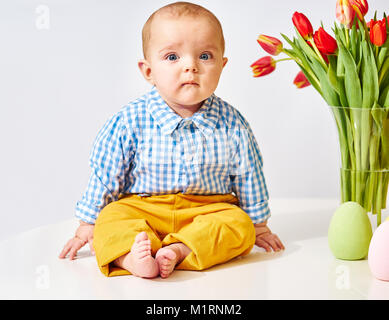 Cute boy sitting next to vase with tulips Stock Photo