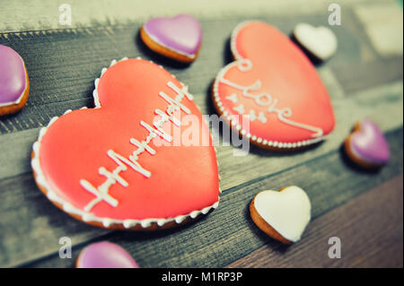 Gingerbread in the shape of heart decorated with red glaze and a pattern in the form of a cardiogram on a wooden background. Stock Photo