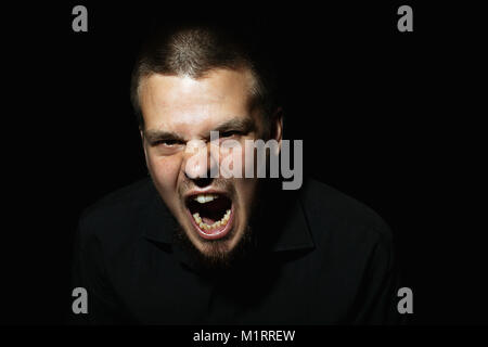 Scared face of spooky man in the dark. The man is yelling Stock Photo