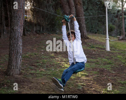 Child playing and sliding on a zip line between two trees in his garden Stock Photo