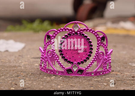 Discarded Birthday Princess Crown on a sidewalk with dumpster and litter blurred in the bokeh. Stock Photo