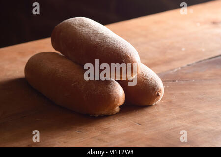 Fresh golden-brown, flour-dusted french rolls stacked on a wooden table Stock Photo