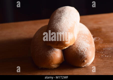 Fresh golden-brown, flour-dusted french rolls stacked on a wooden table Stock Photo