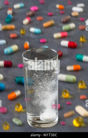 Effervescent tablet in water with bubbles with Multicolored Pills and Capsules on grey slate background Stock Photo