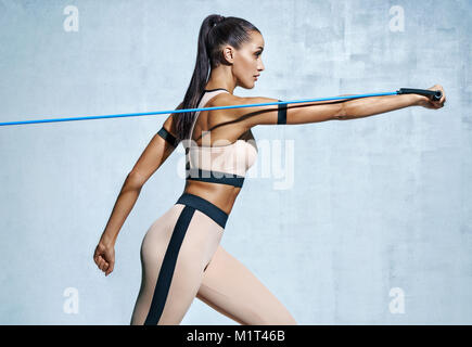 Strong woman using resistance band in her exercise routine. Photo of fitness model workout on grey background. Strength and motivation Stock Photo