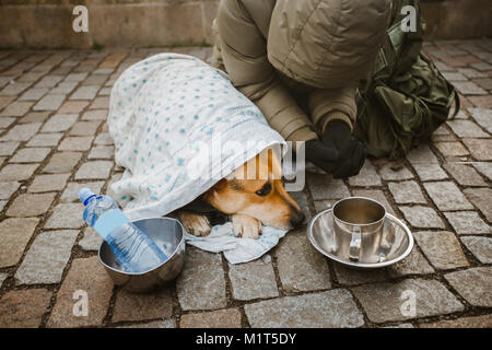 Social theme. A beggar beggar begging with a dog wrapped in a blanket to ask for help in the city of Prague is winter cold. Empty post and bottle with Stock Photo