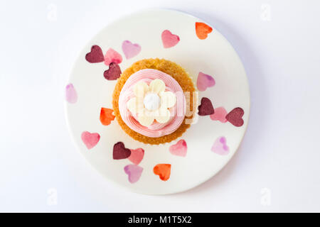 home made cupcake cake with strawberry pink frosting icing and rice paper edible daisy flower, on plate with hearts on isolated on white background Stock Photo